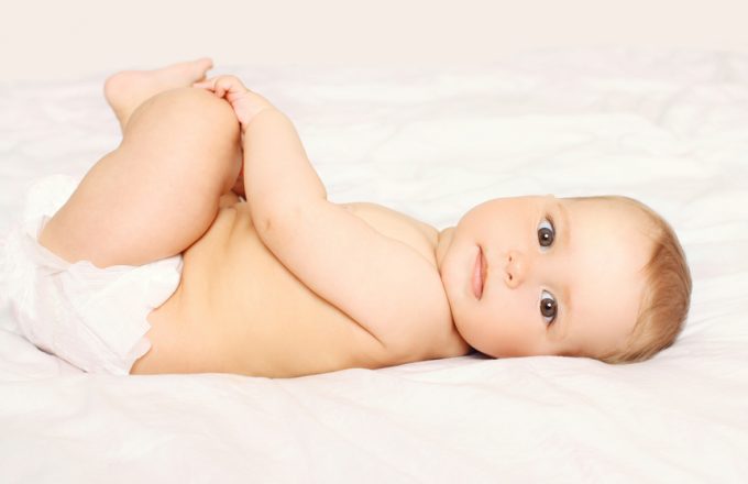 Portrait of cute baby in diapers lying on the bed at home